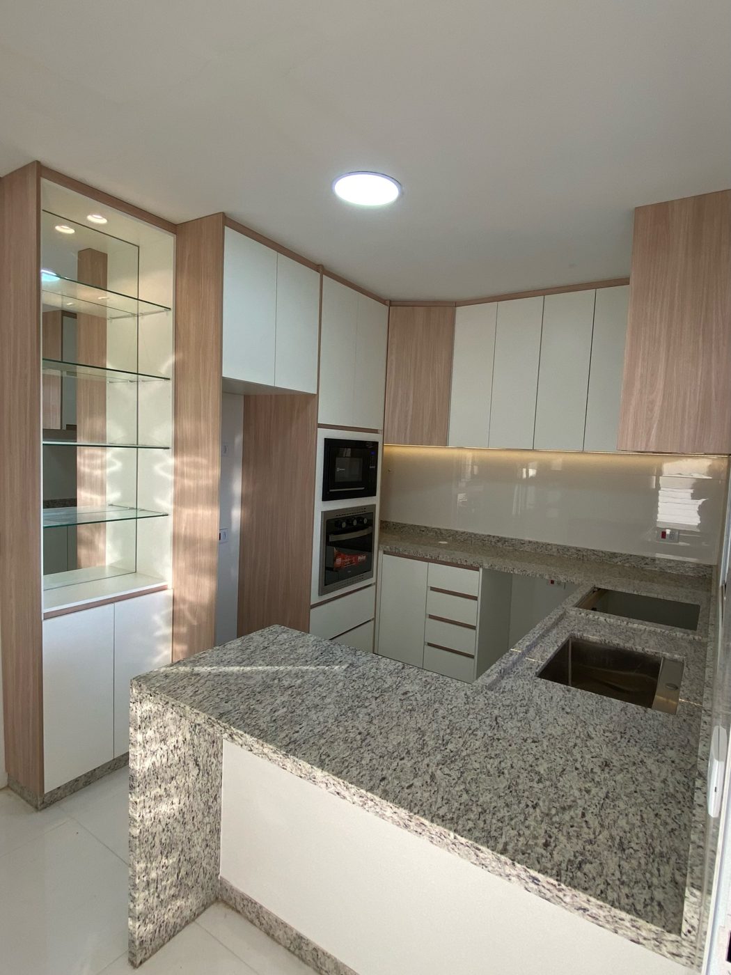 Cozinha planejada com cristaleira de vidro, armários amadeirados e brancos e bancada de granito, feita pela Flake Sky